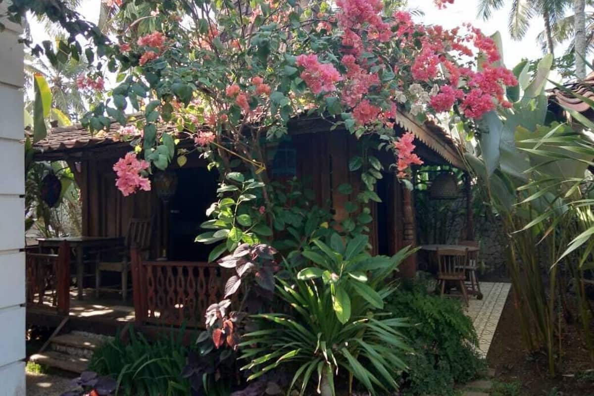 Uma casa de madeira com varanda, rodeada por vegetação exuberante e plantas floridas.