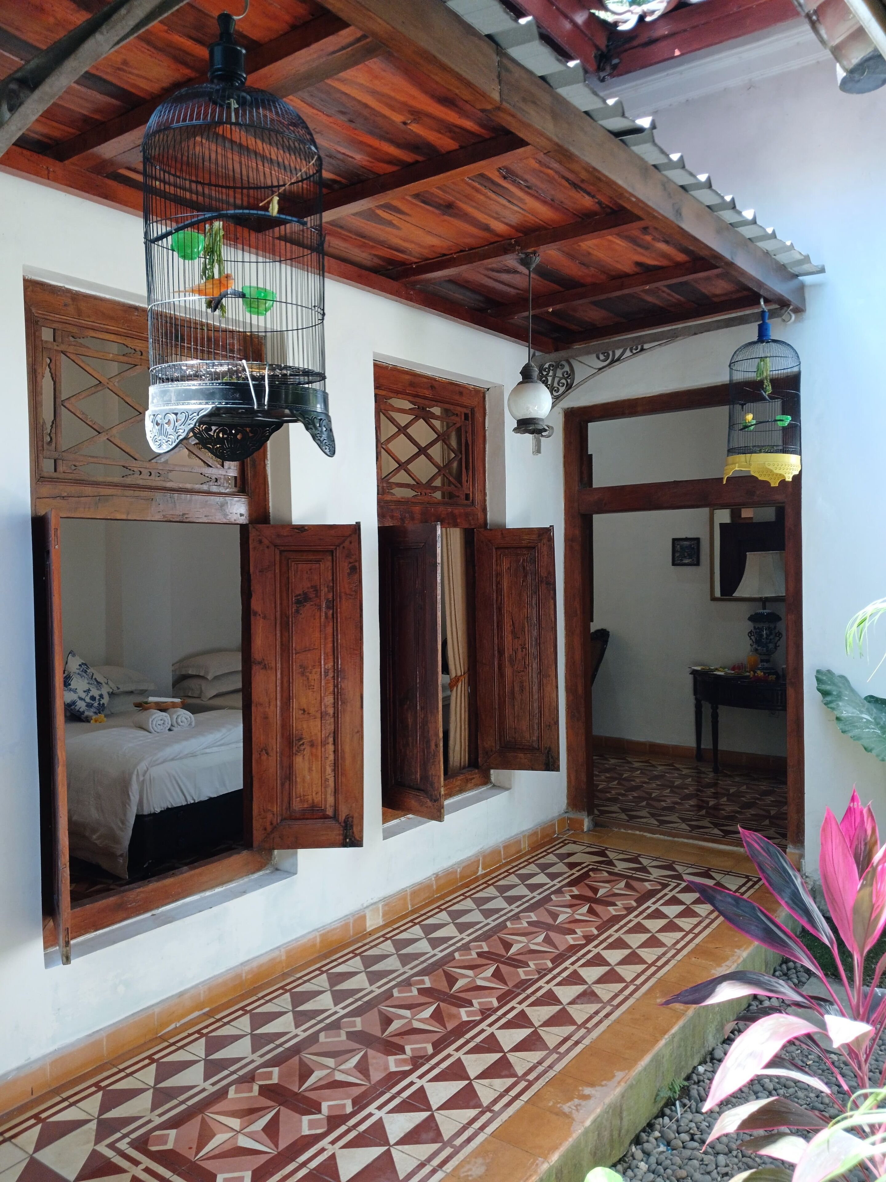 Una habitación tradicional con vigas de madera, suelo de baldosas y una cama con colcha blanca.