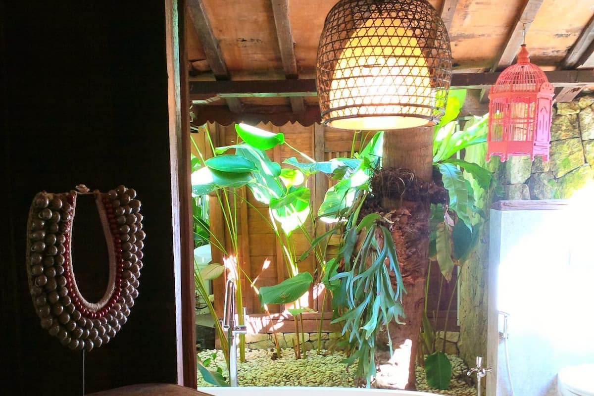Casa de banho com banheira branca, uma prateleira de madeira com um objeto decorativo e plantas penduradas.