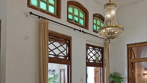 Ein Zimmer mit zwei Betten, einer Kristalllüster und Fenstern mit Holzrahmen und grün getöntem Glas.