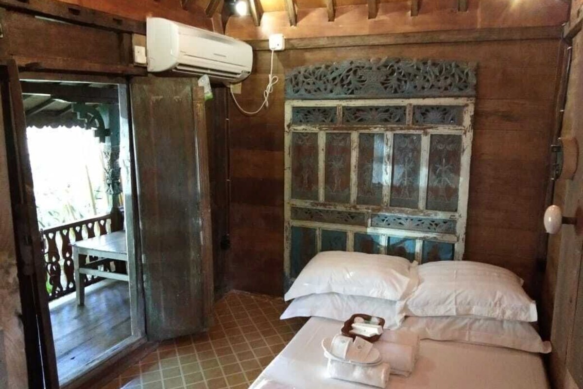 Une pièce en bois avec un lit, une fenêtre ornée d’un cadre décoratif et un appareil de climatisation.