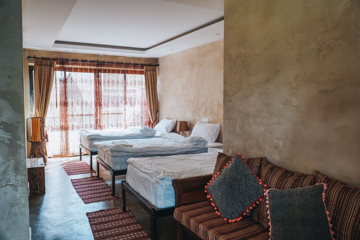 A hotel room with two beds, a sofa, and a large window with curtains.