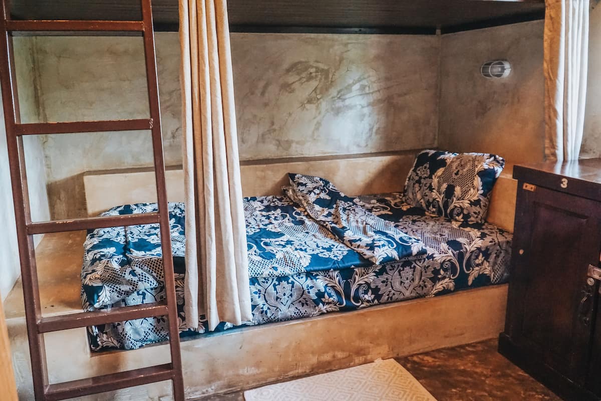 A room with a bed, a wooden ladder, a wall with a textured pattern, and a small cabinet.