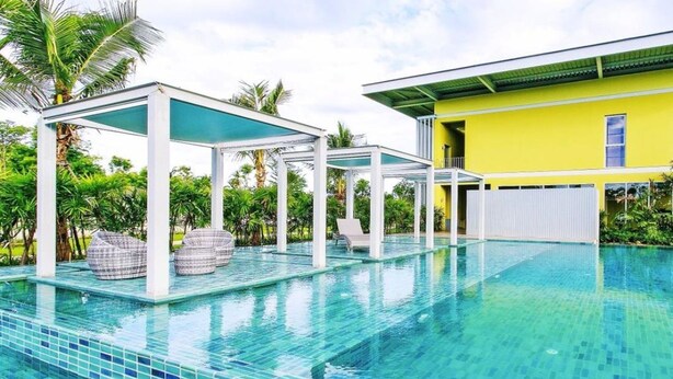 A swimming pool with clear blue tiles, white pillars, and outdoor seating. - Villa Meesuk Residence (San Sai)