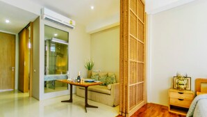 A modern hotel room with a wooden floor, a sofa, a small table, a nightstand, and a large window. - Villa Meesuk Residence (San Sai)