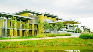 A modern building with a flat roof, a reflective water feature in front, and a well-maintained lawn. - Villa Meesuk Residence (San Sai)