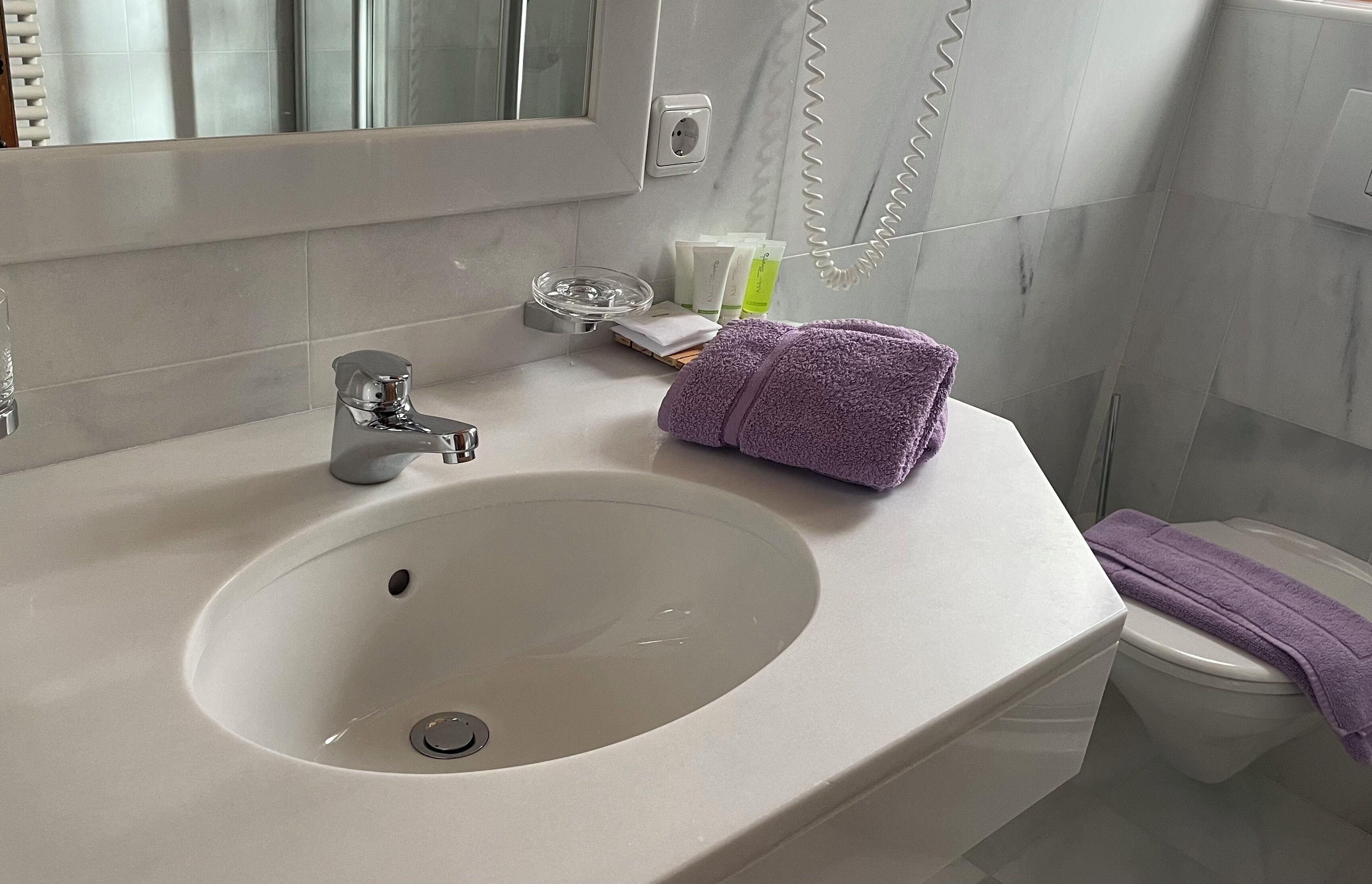 A bathroom with a white sink, a mirror, a toilet, and a towel on the counter.