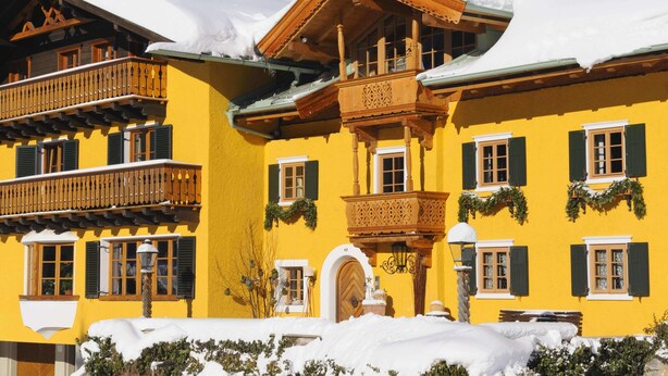 A yellow building with wooden balconies and green shutters, surrounded by snow. - Chalet Brunnenhof (Sankt Anton am Arlberg)