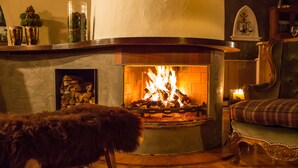 A cozy living room with a fireplace, a fur-covered chair, and a plaid sofa. - Chalet Brunnenhof (Sankt Anton am Arlberg)