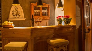 A wooden bar area with two stools, a wine bottle, and glasses. - Chalet Brunnenhof (Sankt Anton am Arlberg)