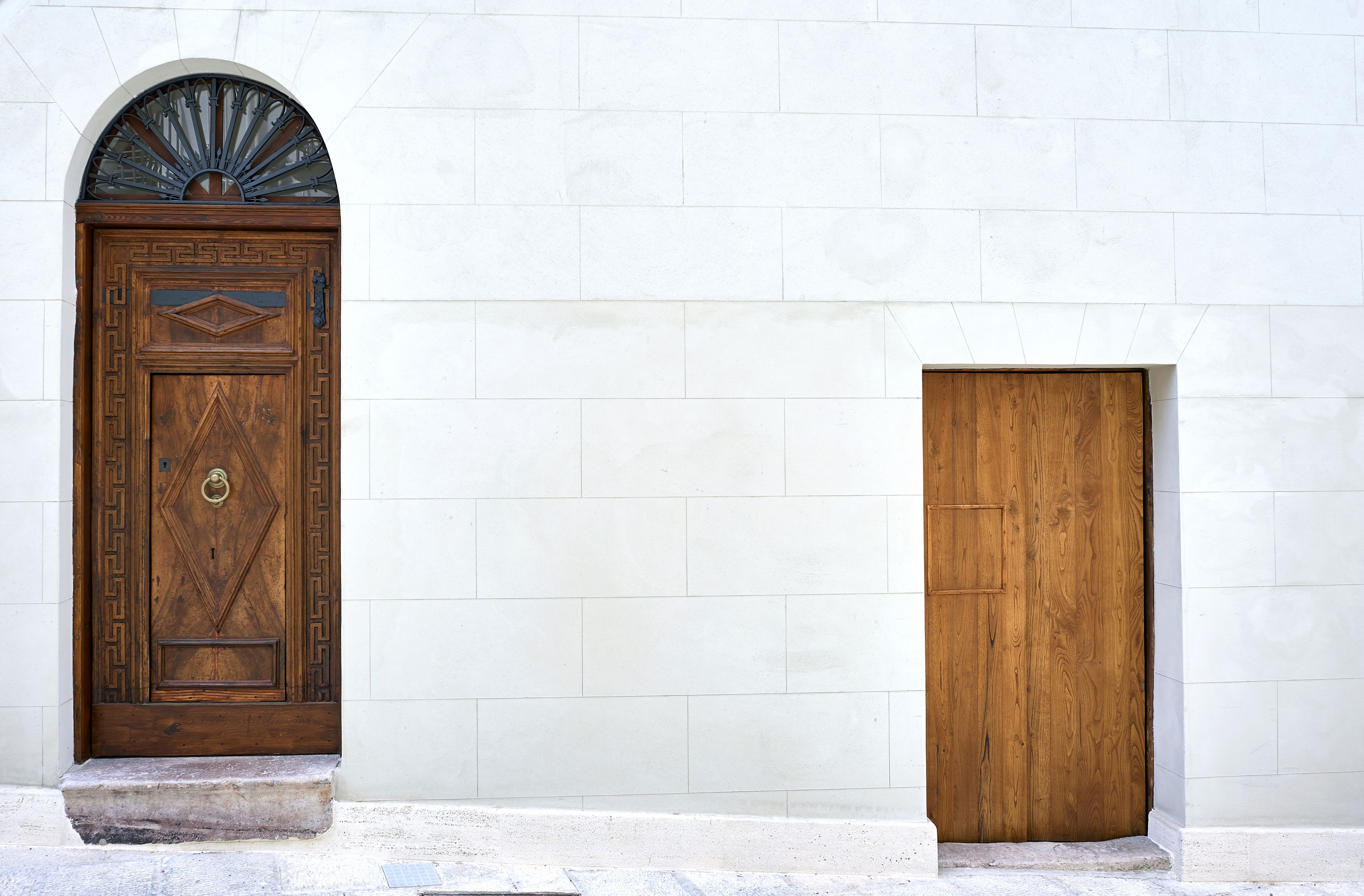 Deux portes en bois aux motifs différents : l’une est surmontée d’une arche décorative, l’autre présente un simple linteau. Elles sont placées devant un mur recouvert de carreaux blancs.