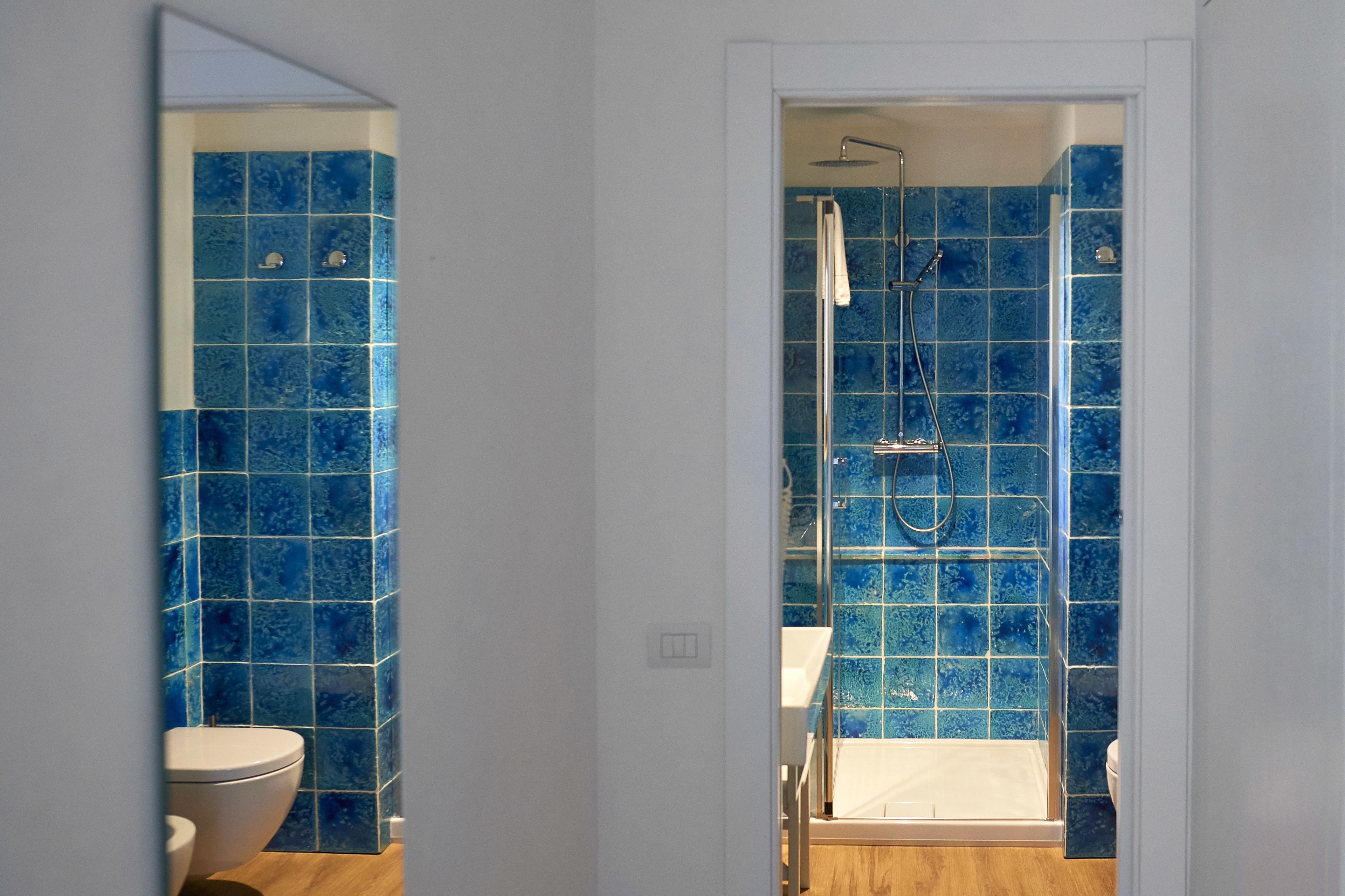 A bathroom with blue tiles, a shower, and a toilet.