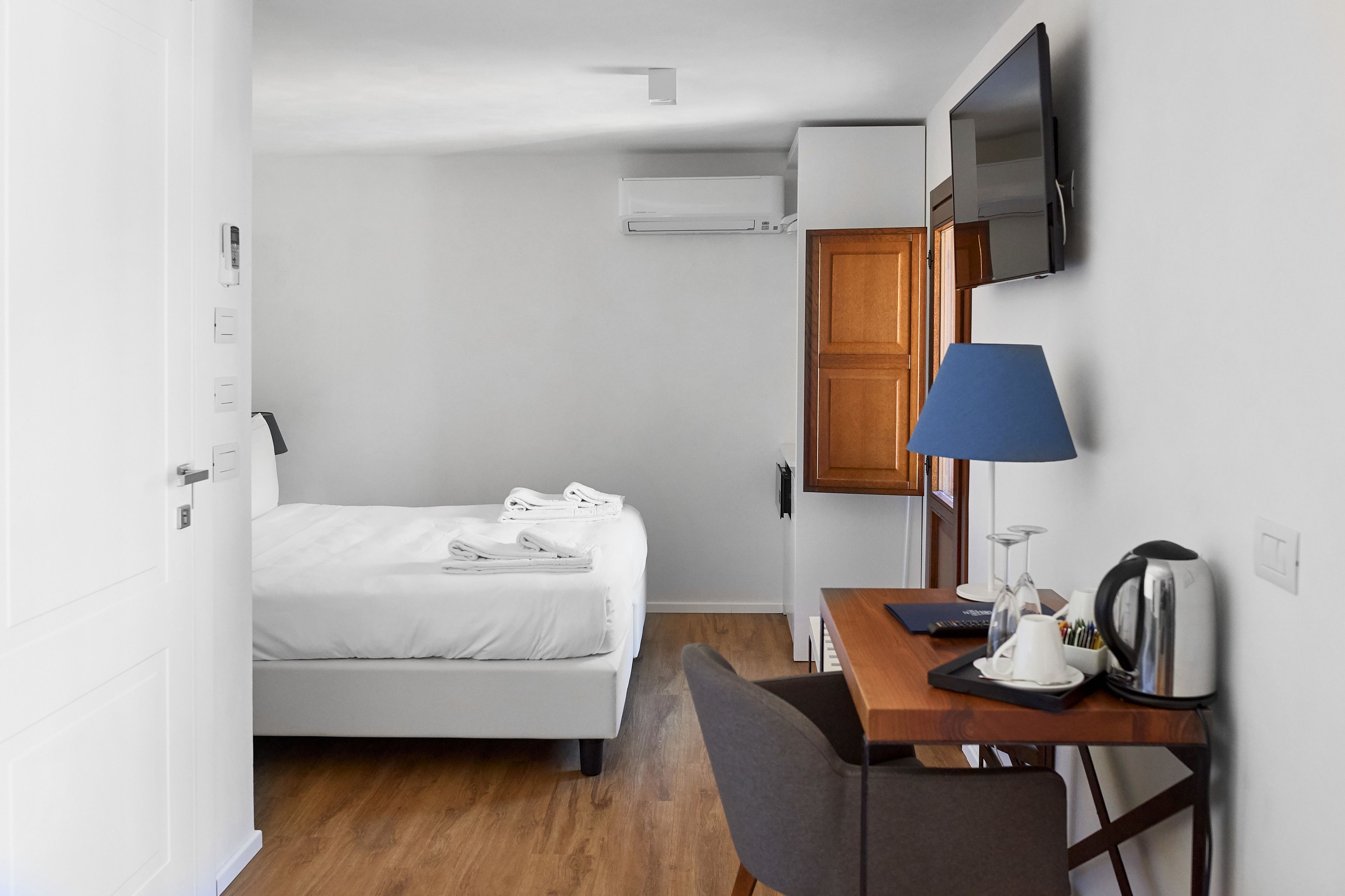 Une chambre d’hôtel équipée d’un lit, d’un bureau avec une lampe, d’une bouilloire et d’un téléviseur fixé au mur.