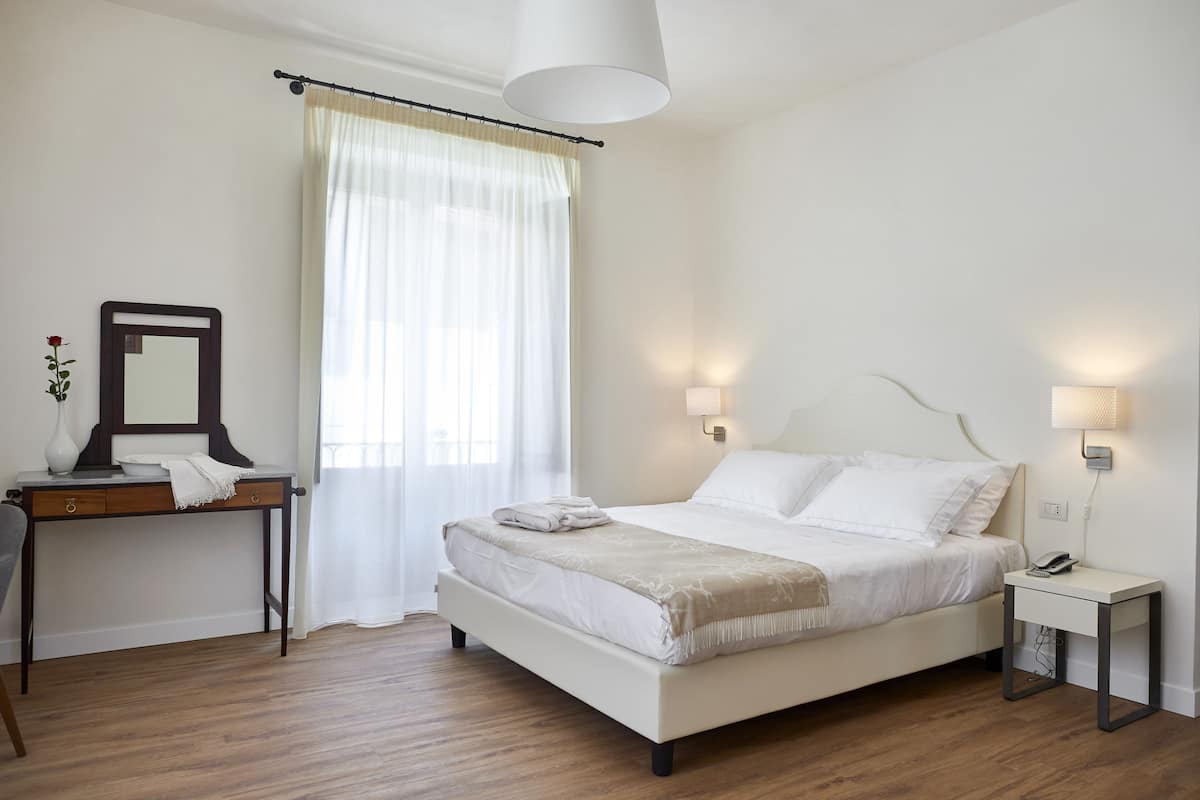A bedroom with a bed, bedside table, lamp, and a mirror on a dresser.