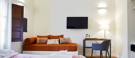 Habitación de hotel con cama, escritorio, silla, televisor de pantalla plana y lámpara.