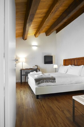 A hotel room with a wooden ceiling, a bed with white bedding, a desk with a lamp, and a TV on the wall. - Hotel Sopra Le Mura (Castellammare del Golfo)
