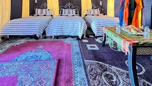 Ein Zimmer mit drei Betten, einem Tisch mit Wasserflaschen und einem farbenfrohen Teppich.