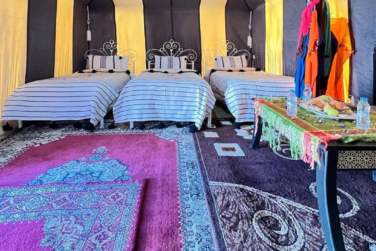 Ein Zimmer mit drei Betten, einem Tisch mit Wasserflaschen und einem farbenfrohen Teppich.