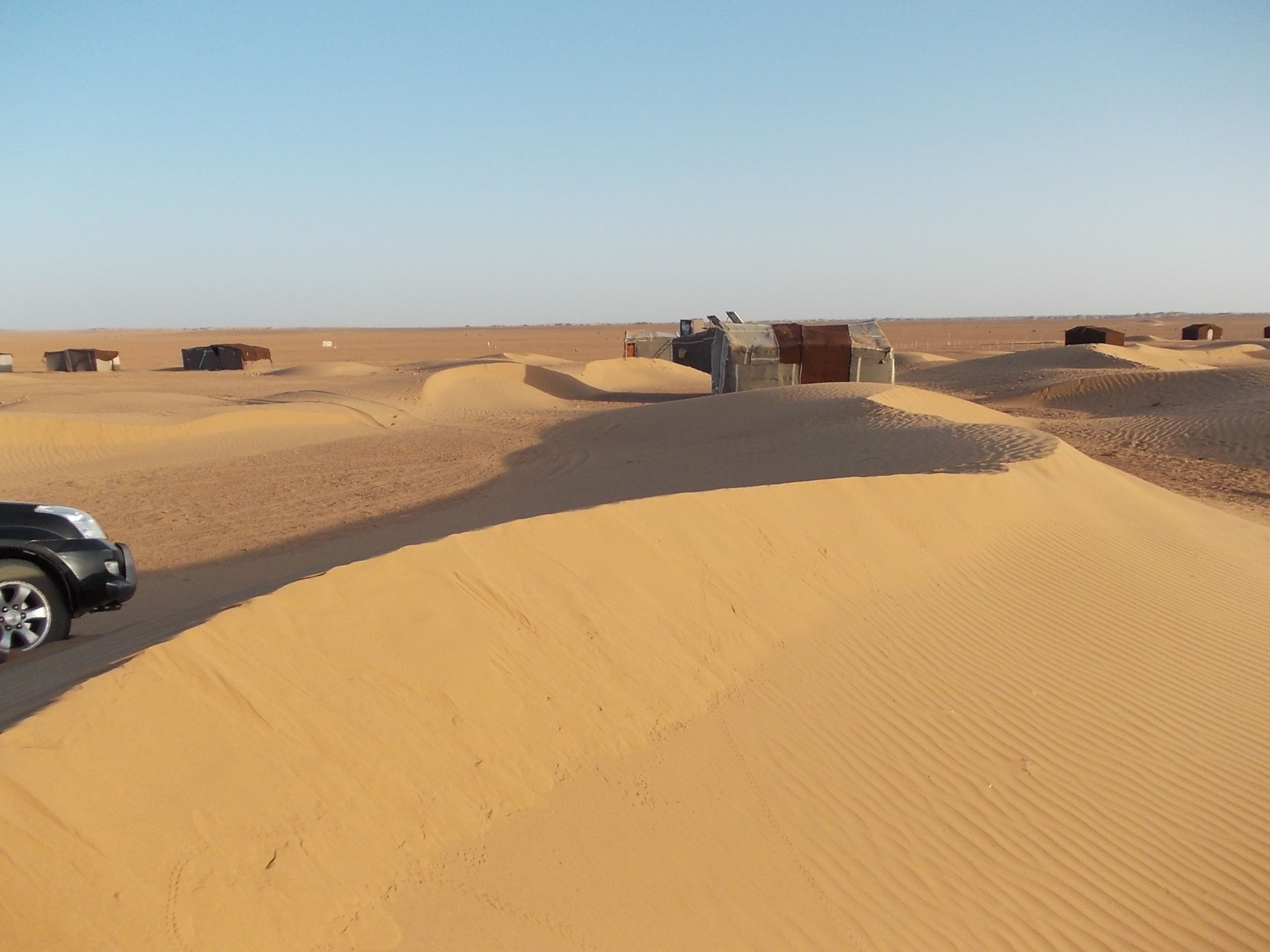 Paisaje desértico con dunas de arena y pequeñas construcciones.
