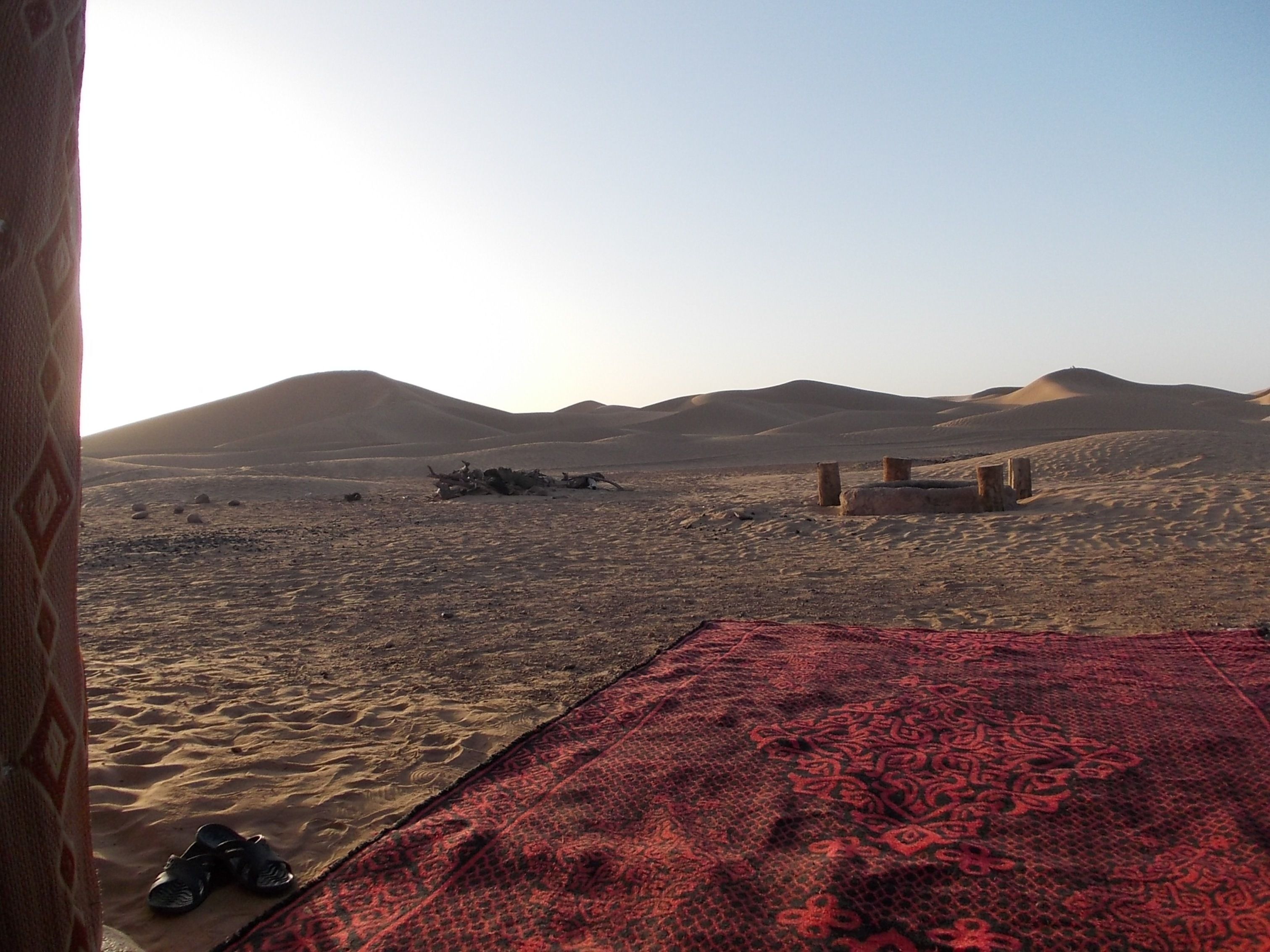A desert landscape with sand dunes and a red patterned rug on the ground.