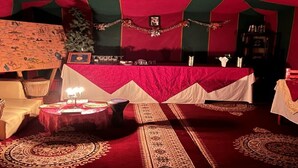 Ein zeltartiges Zimmer mit rotem und grünem Farbton, ein Tisch mit weißer Tischdecke und gemusterte Teppiche auf dem Boden.