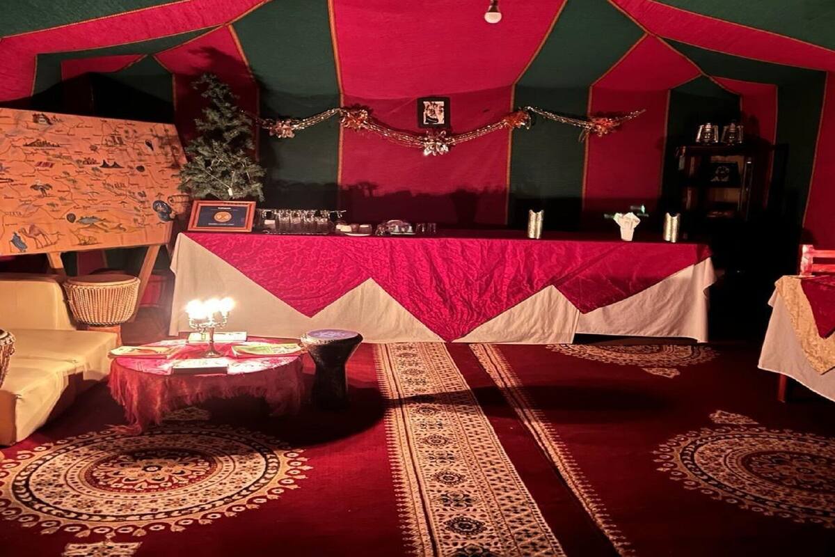 Ein zeltartiges Zimmer mit rotem und grünem Farbton, ein Tisch mit weißer Tischdecke und gemusterte Teppiche auf dem Boden.
