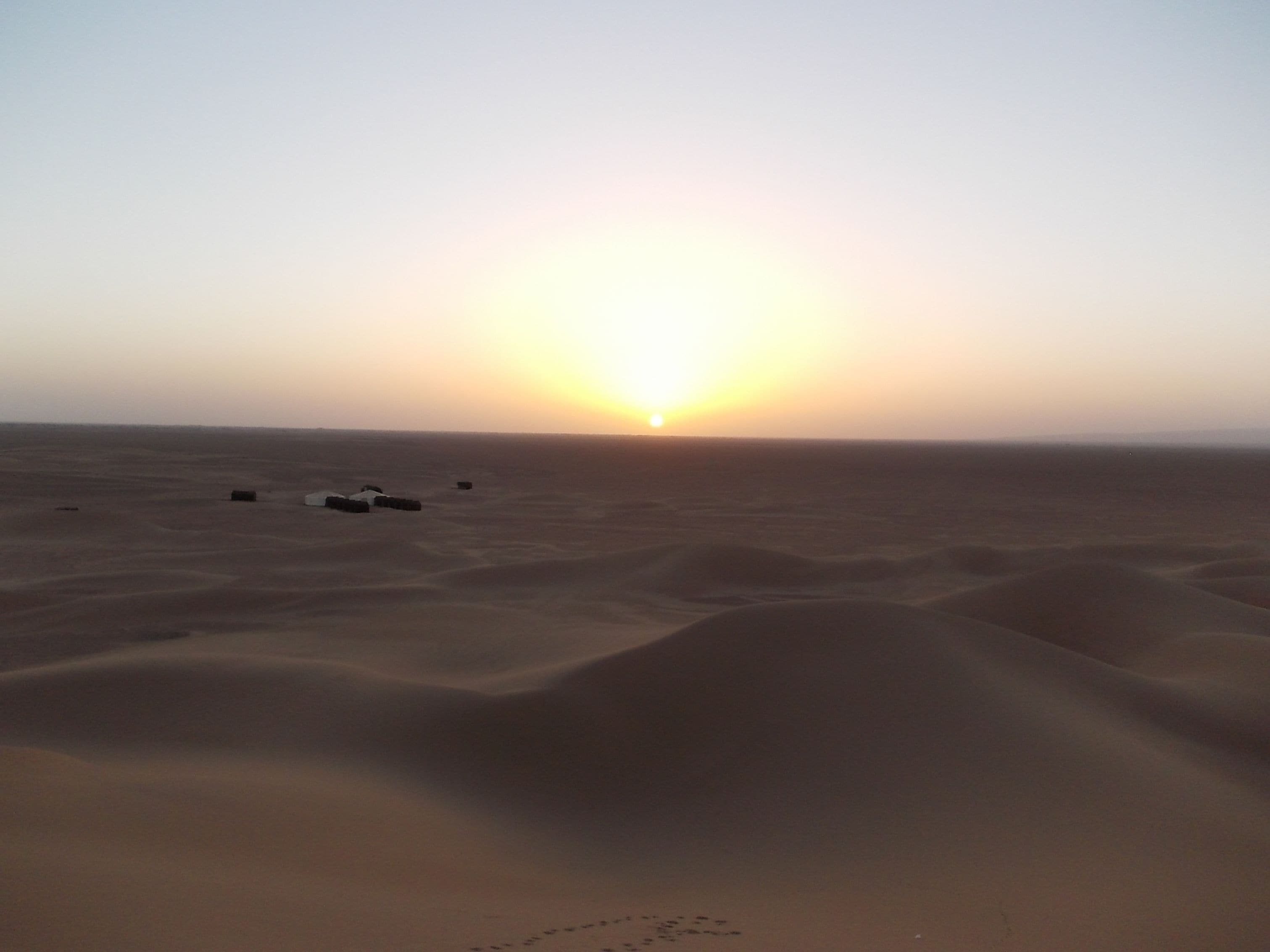 A desert landscape with sand dunes and a sunset.