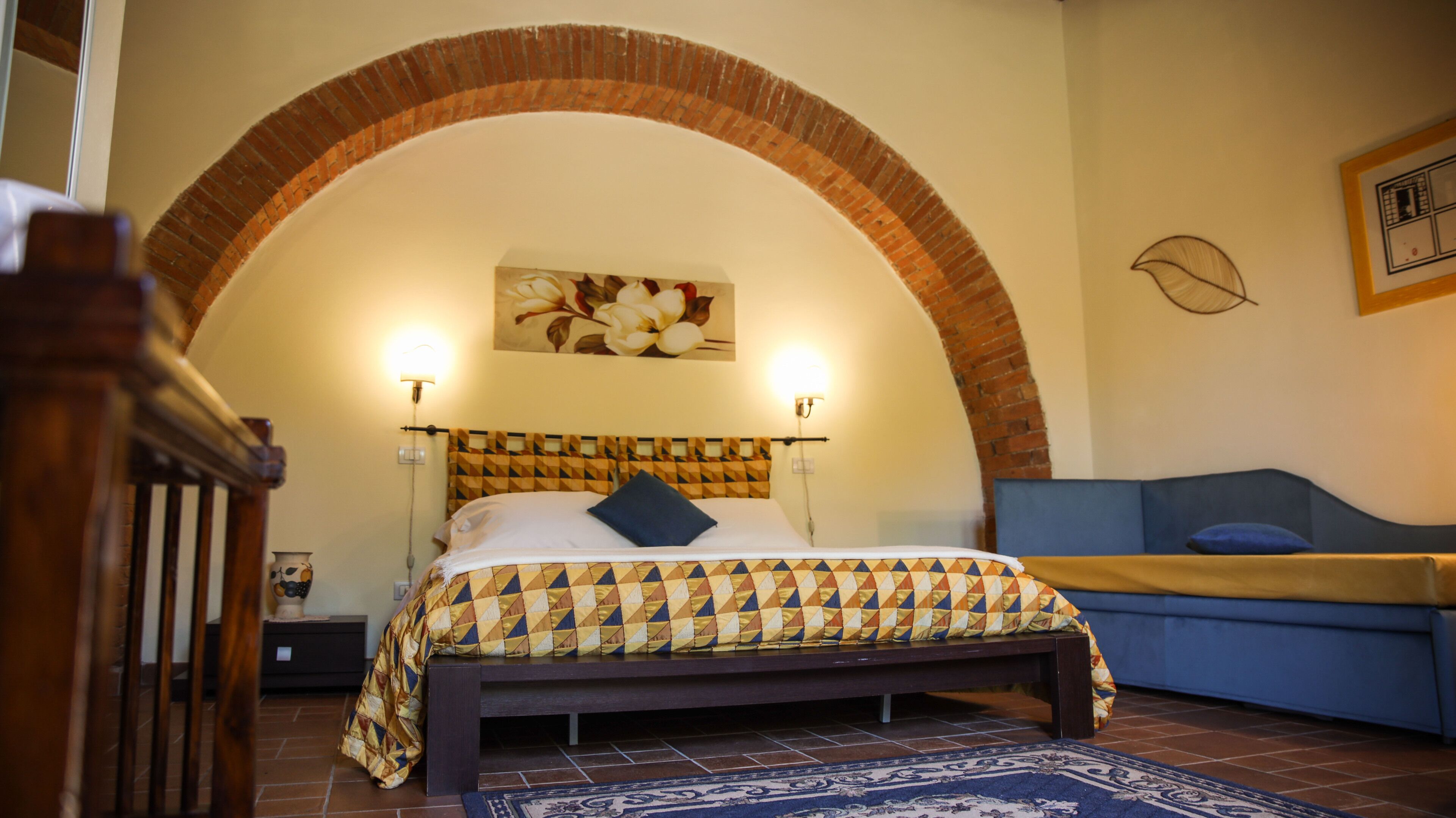 Un dormitorio con cama, un sofá azul, cabecera estampada y un arco decorativo.