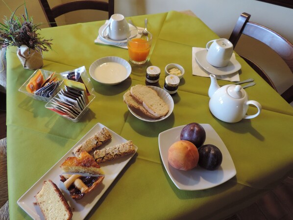 Una mesa de desayuno con una variedad de alimentos, incluyendo pan, bollería, frutas y bebidas.