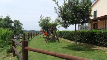Explore a serene outdoor space with a grassy path, children's play area, and beautifully manicured hedges and trees.