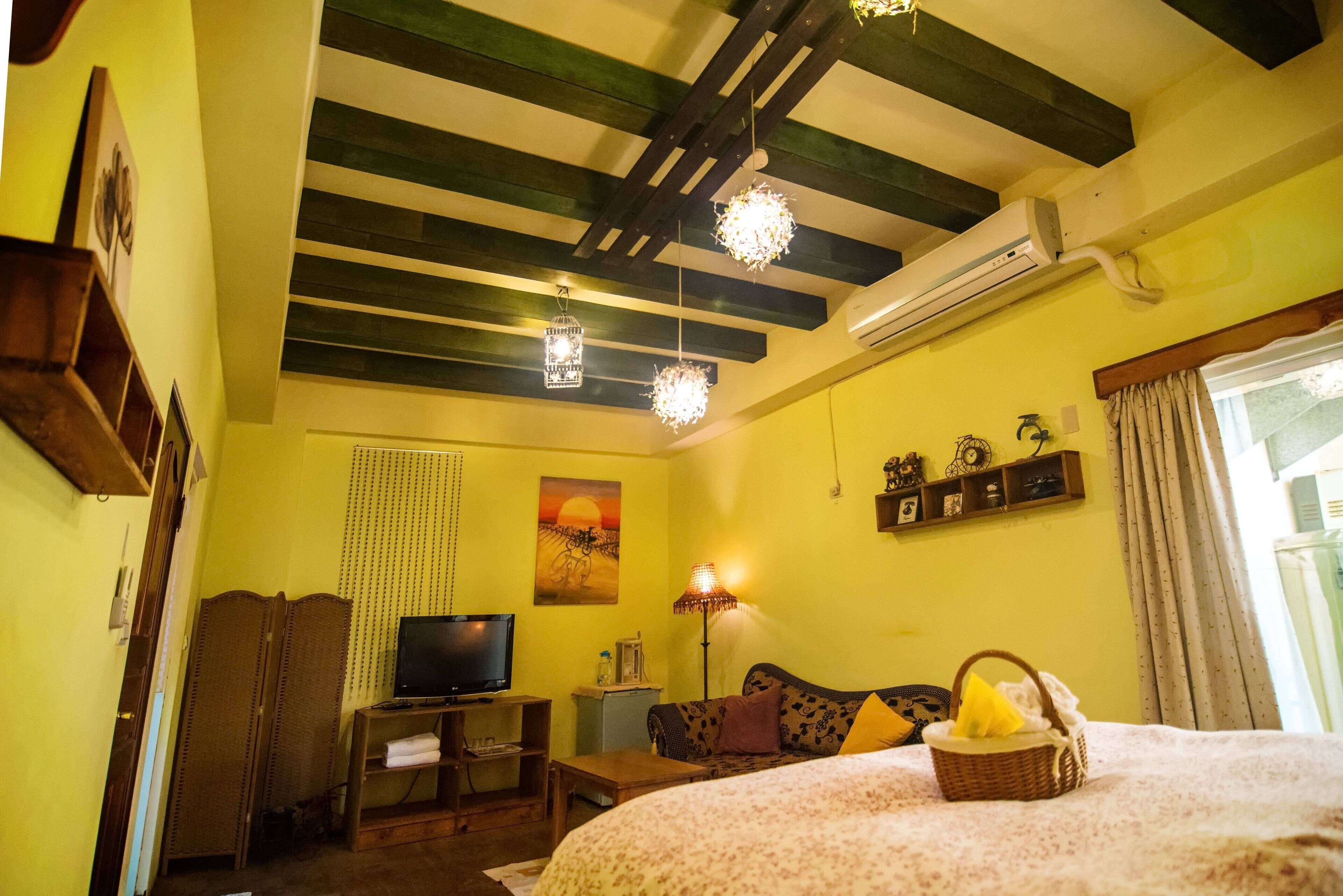 A room with a bed, a television, a lamp, and a shelf with decorative items.
