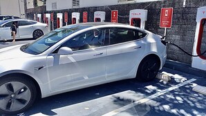 Ein weißes Tesla Model S wird an einer öffentlichen Ladestation mit mehreren Ladeanschlüssen aufgeladen.