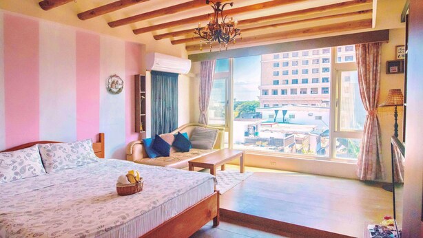 Ein Schlafzimmer mit Bett, einer Couch, einem Fenster mit Blick auf Gebäude und einer Chandelier.