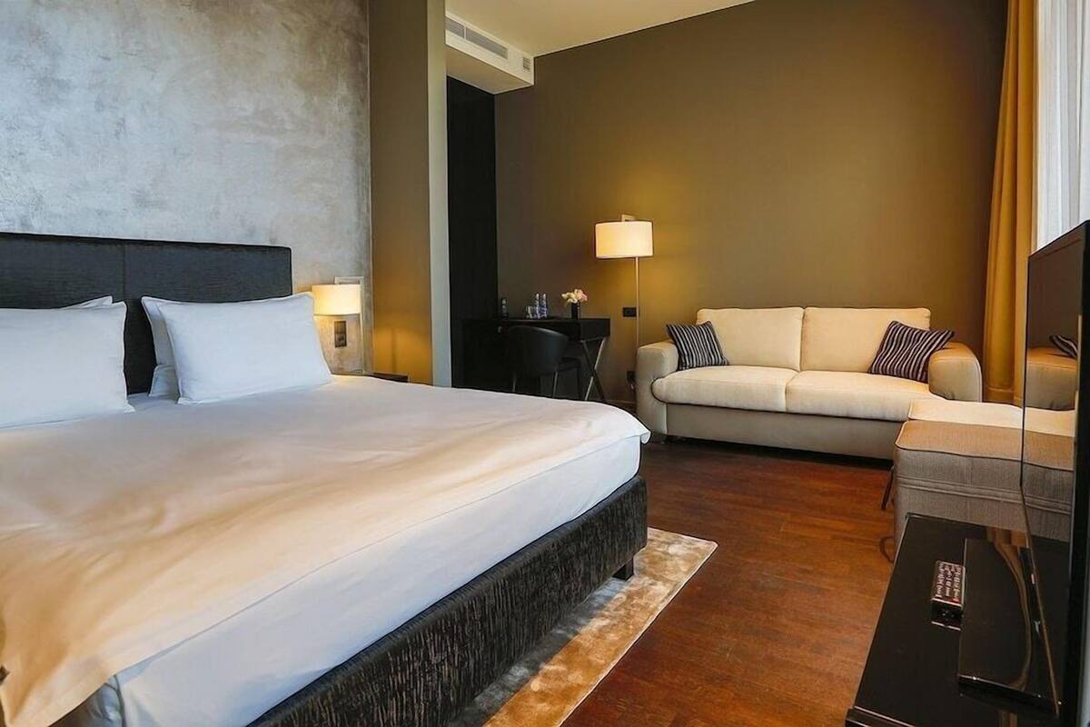 A hotel room with a large bed, a sofa, a desk, and a lamp.