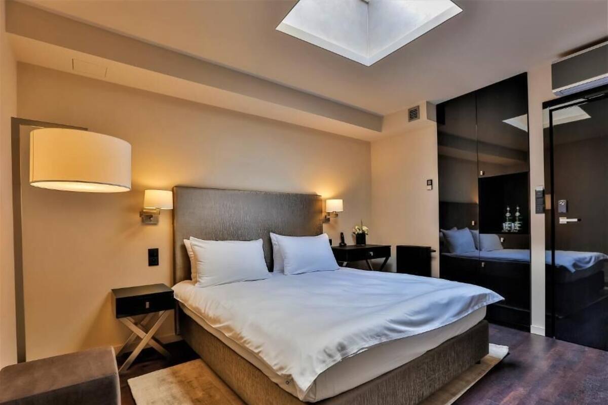A modern bedroom with a large bed, bedside lamps, a skylight, and a wardrobe.