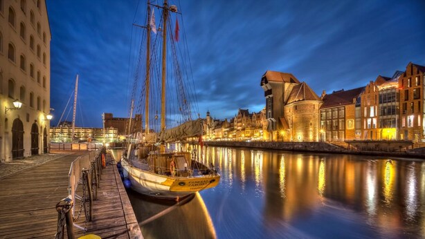A historic canal with a tall ship docked at a wooden pier, surrounded by traditional European architecture. - Medusa Gdańsk (Gdansk)