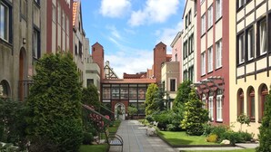A courtyard with a central pathway flanked by buildings with traditional architecture, including arched windows and brick chimneys. - Medusa Gdańsk (Gdansk)