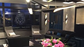 A modern lounge area with a sofa and chairs, a table with a floral arrangement, and a wall with a logo. - Medusa Gdańsk (Gdansk)