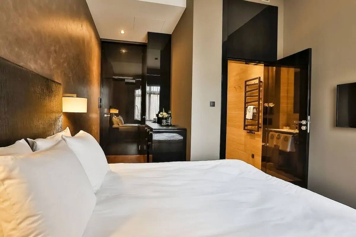 A hotel room with a large bed, a desk, a chair, a lamp, and a bathroom visible through an open door.