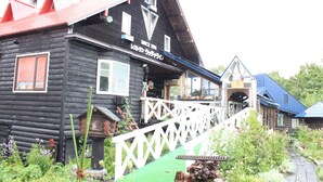 A log cabin with a red roof, a porch with a white railing, and a sign that reads "Since 1933". - Woody Life (Kamifurano)
