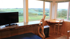 A room with a bed, a TV, a chair, and a large window offering a view of the countryside. - Woody Life (Kamifurano)
