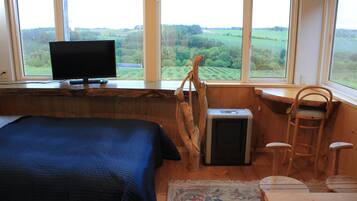 A bedroom with a bed, a television, a window with a view of the countryside, a chair, and a small table.