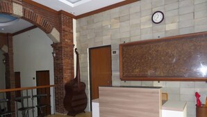 A reception area with a wooden reception desk, a clock on the wall, and a large framed artwork above the desk. - Jacatra Homestay (Malang)
