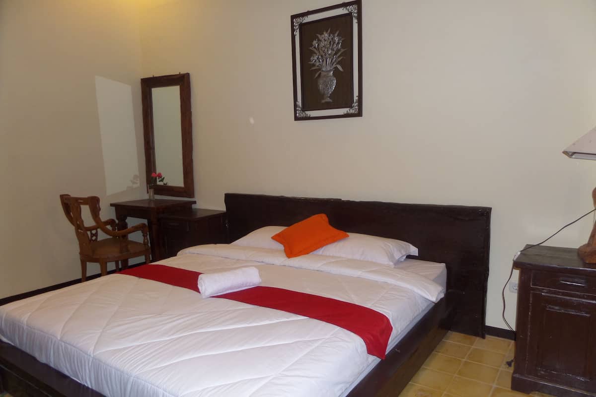 A neatly made bed with a red and white bedspread, a wooden nightstand with a lamp, a chair, and a framed picture on the wall.