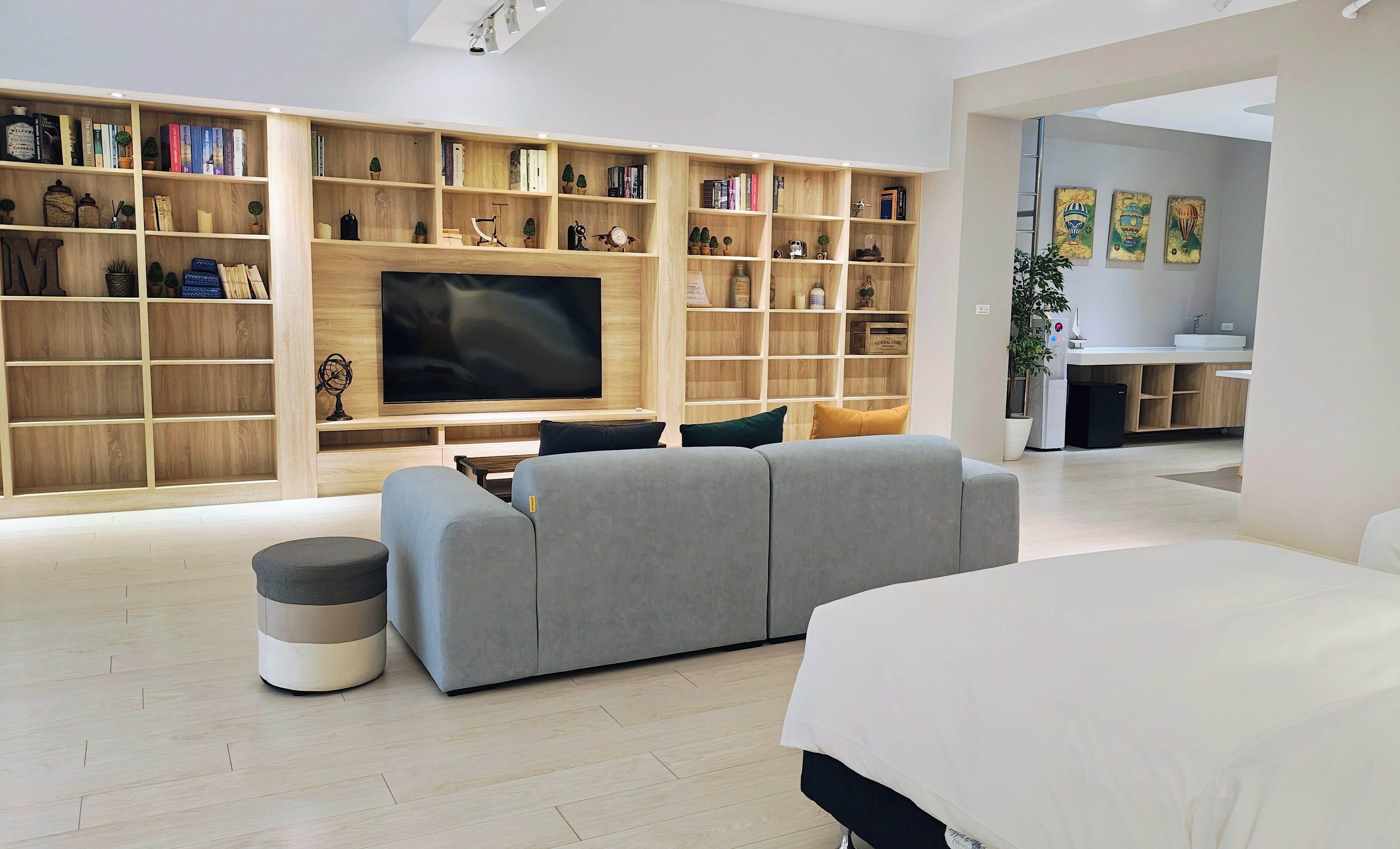 A modern living room with a large flat-screen TV, a grey sofa, and a bookshelf filled with books and decorative items.