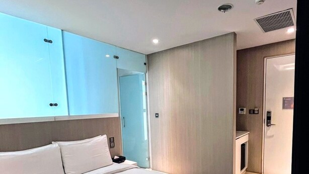 A modern hotel room with a large bed, a wardrobe, a bathroom, and a small seating area.
