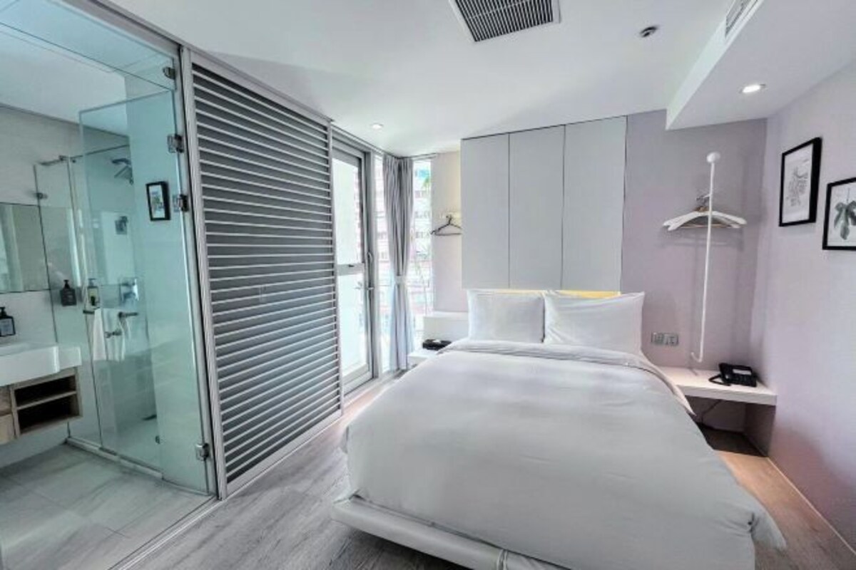 Une chambre à coucher moderne avec un grand lit, une douche en verre et une table de chevet avec un téléphone.