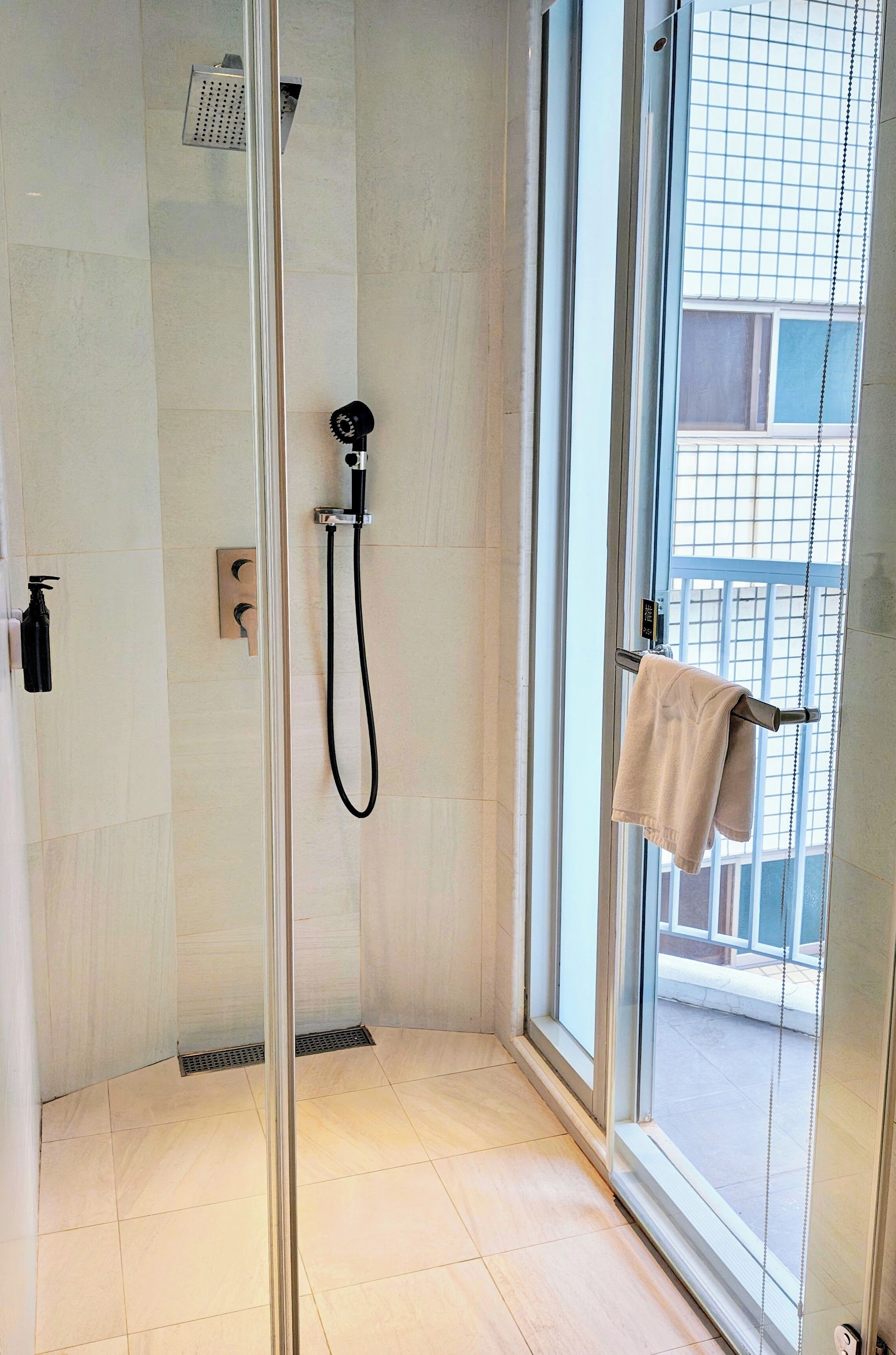 A modern shower with a glass door, a handheld showerhead, and a towel rack with a towel.