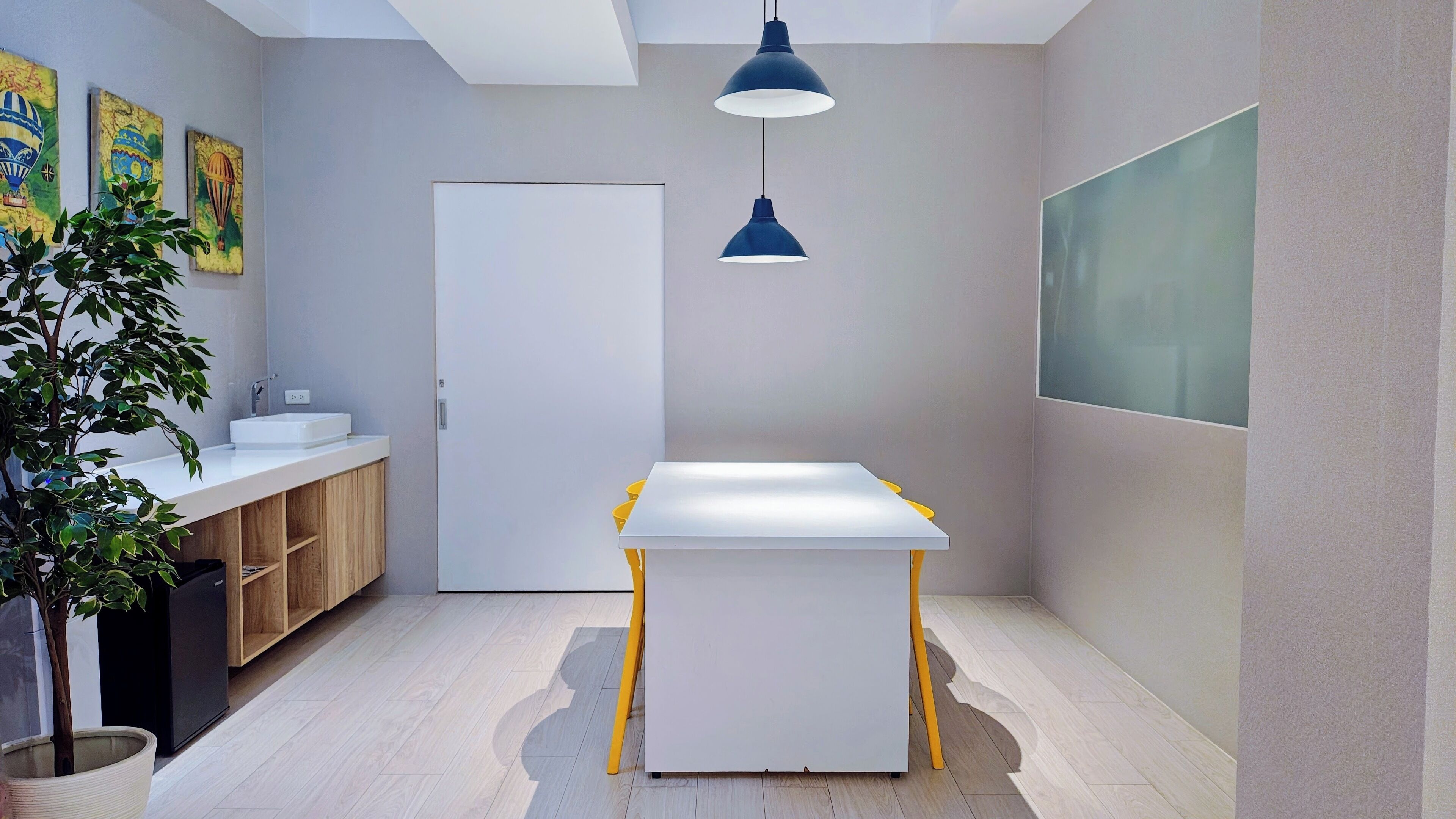 A modern, minimalist room with a white table, yellow chairs, a white sink, and a potted plant.
