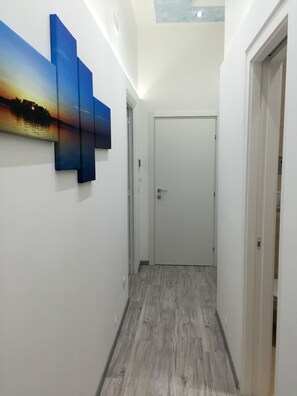 Ein Flur mit Holzboden, einer weißen Tür am Ende und einem Wandbild mit Sonnenuntergang.